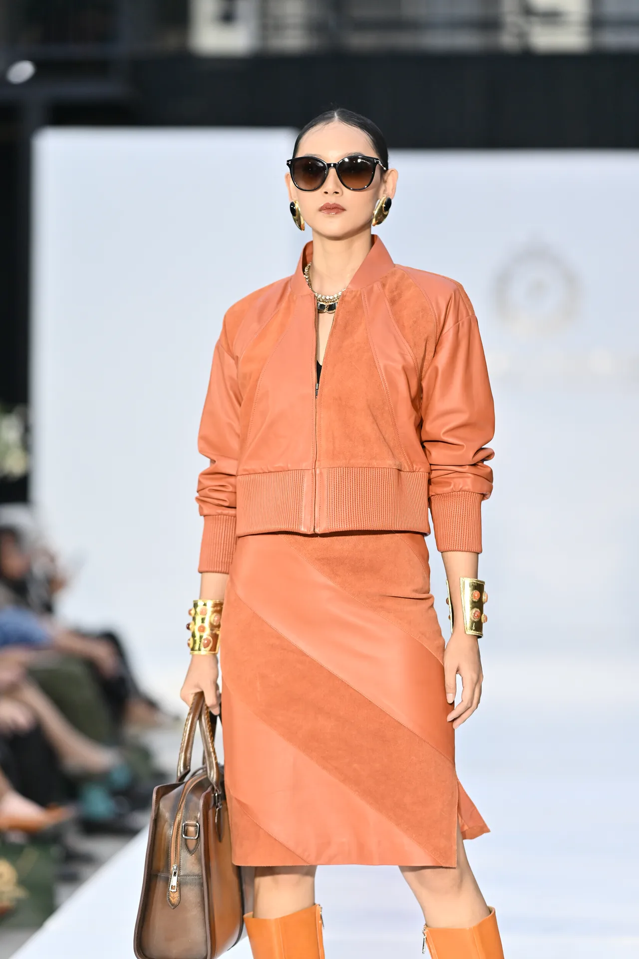 Gina walking in a terracotta leather suit with sunglasses