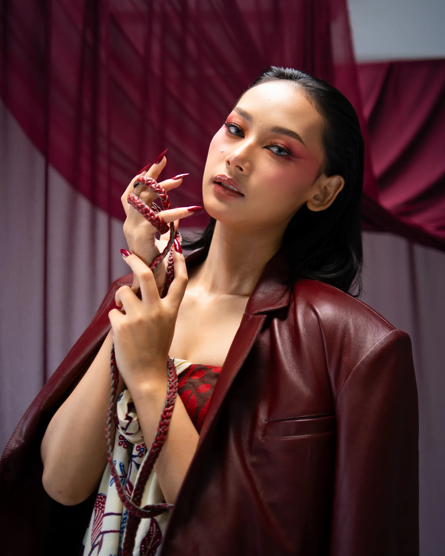 Gina in a burgundy leather blazer holding a sculpted red cord